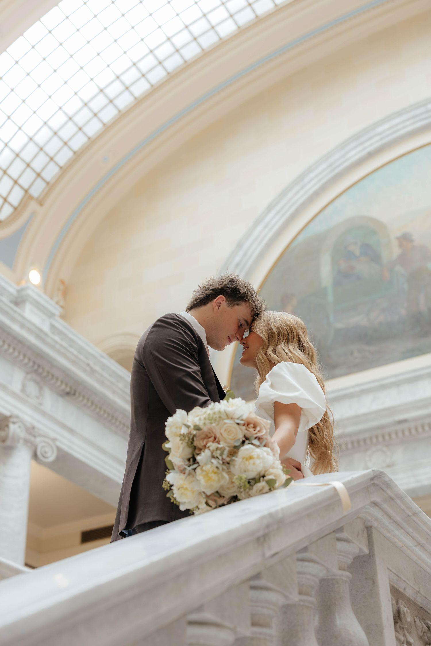 Wedding couple shares kiss outside temple with bride holding white floral bouquet.