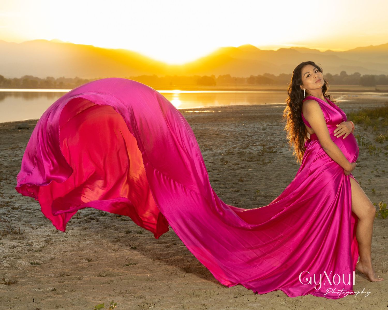 Flowing hot pink dress billowing dramatically against a golden sunset over water.