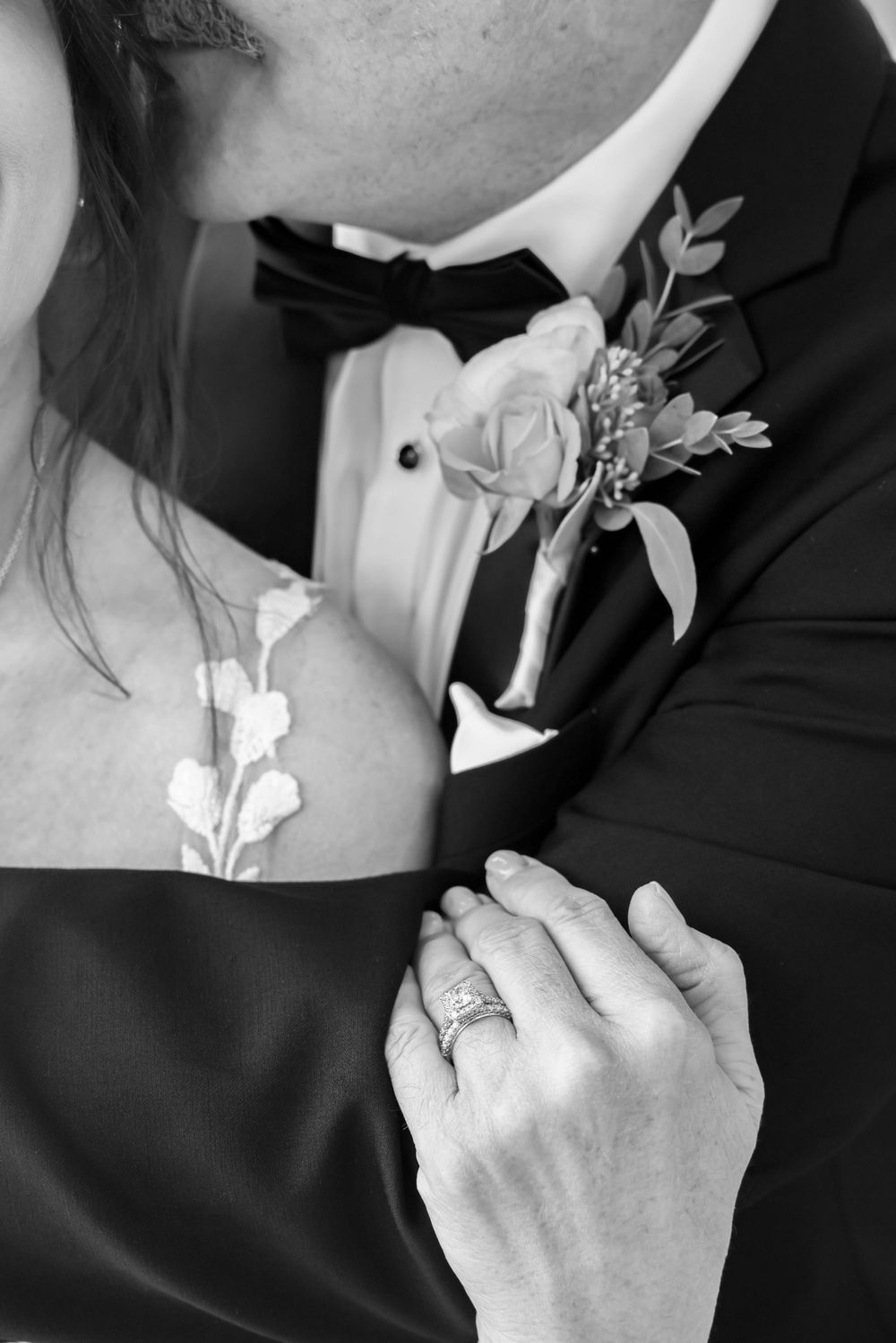 Black and white detail shot of a boutonniere on a groom's lapel with delicate white flowers and greenery.