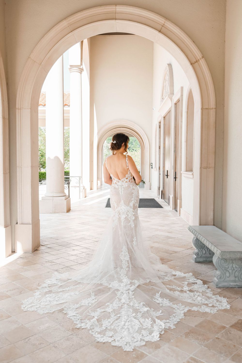 Elegant lace wedding dress with a dramatic train photographed in an arched colonnade.