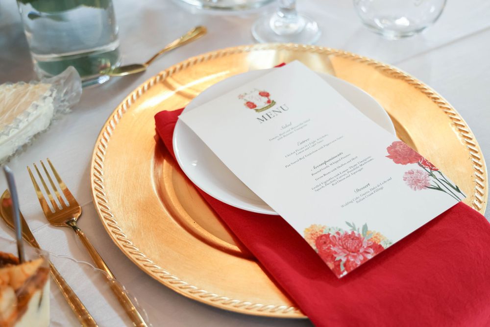 Elegant gold charger plate with red napkin and floral menu card at wedding reception place setting.