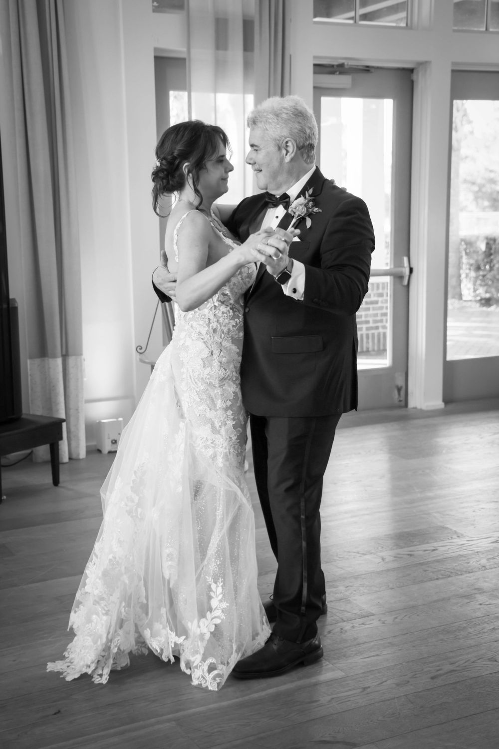 A black and white candid moment of a couple sharing a dance in formal wedding attire.