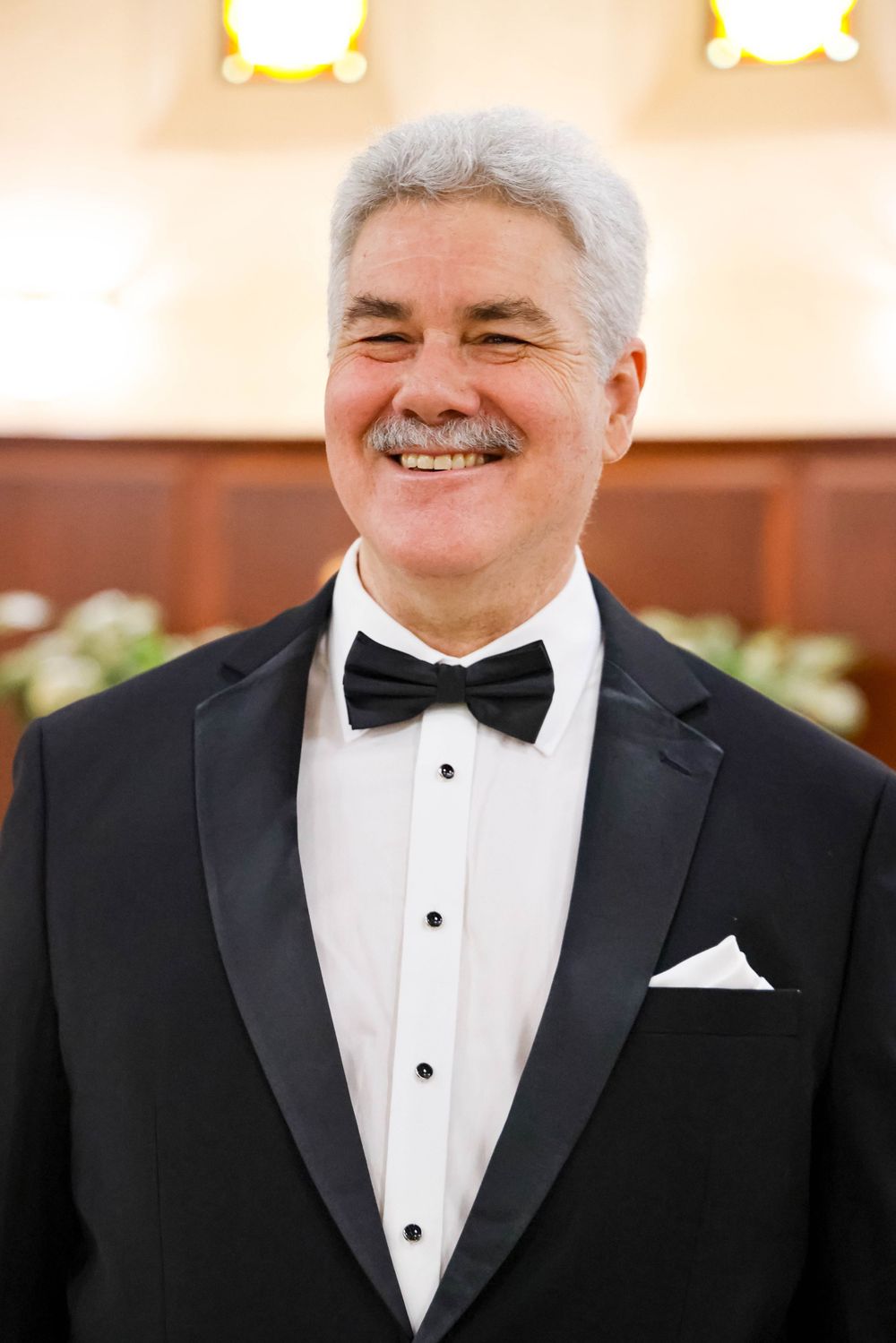 Man in classic black tuxedo and bowtie smiles warmly at wedding event.