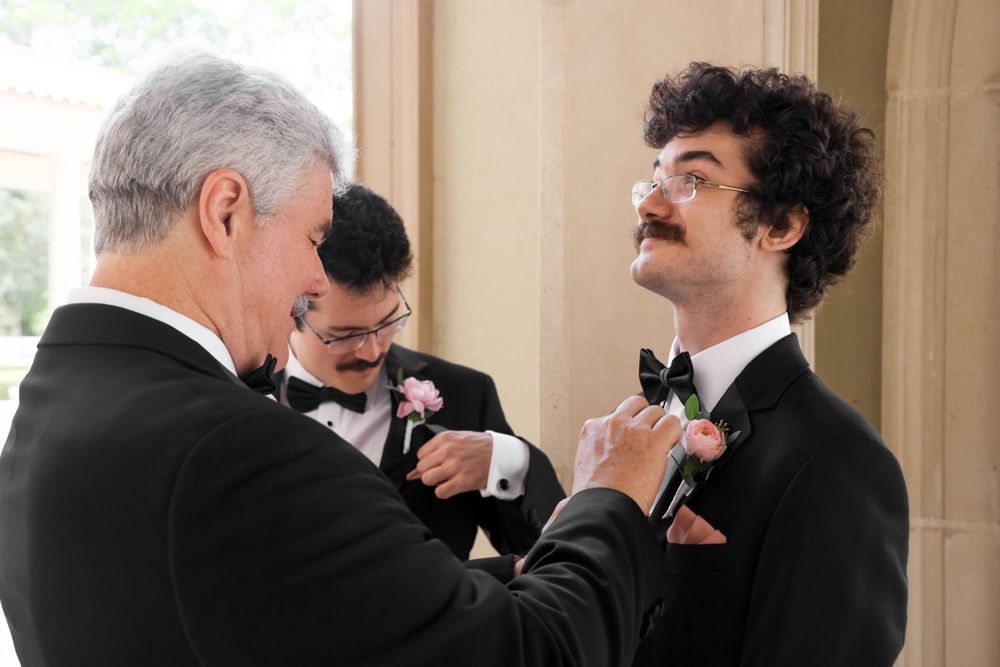 Men in formal attire help adjust each other's boutonnieres before the ceremony.