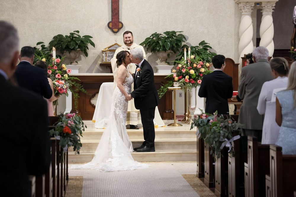 Wedding ceremony in progress at church altar decorated with floral arrangements.