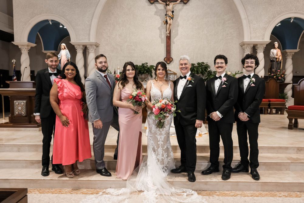 Wedding party poses for formal group photo at church altar with floral decorations.