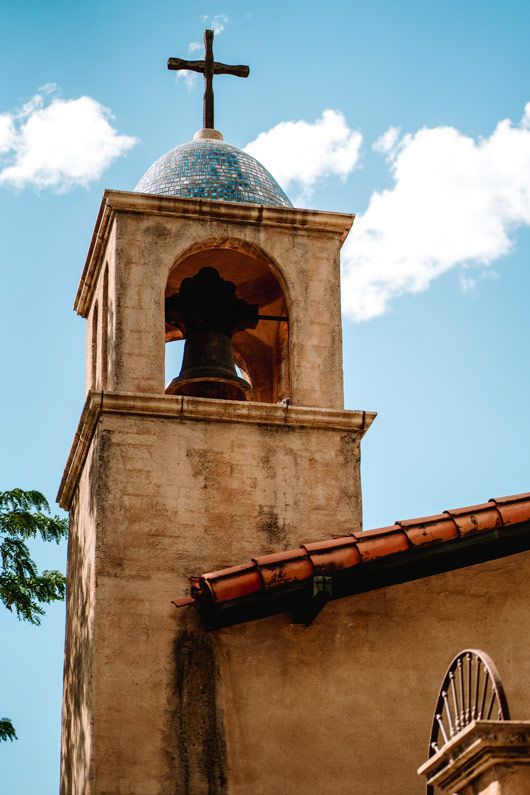 Sedona church bell tower with cross against blue sky with white clouds.
