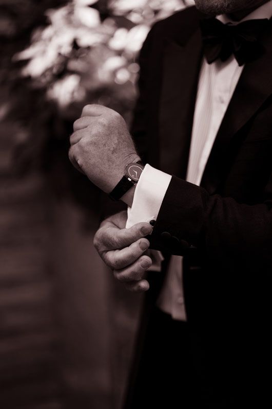 Close up of hands adjusting formal shirt cuffs and watch in black and white.