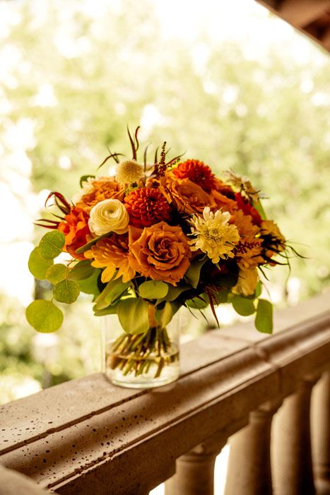 Autumn-colored wedding bouquet with roses and greenery in golden sunlight.