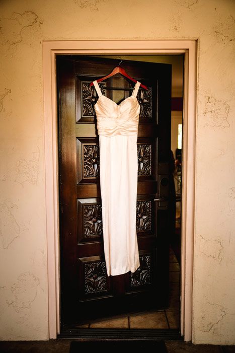 A white wedding dress hanging on an ornate wooden door.