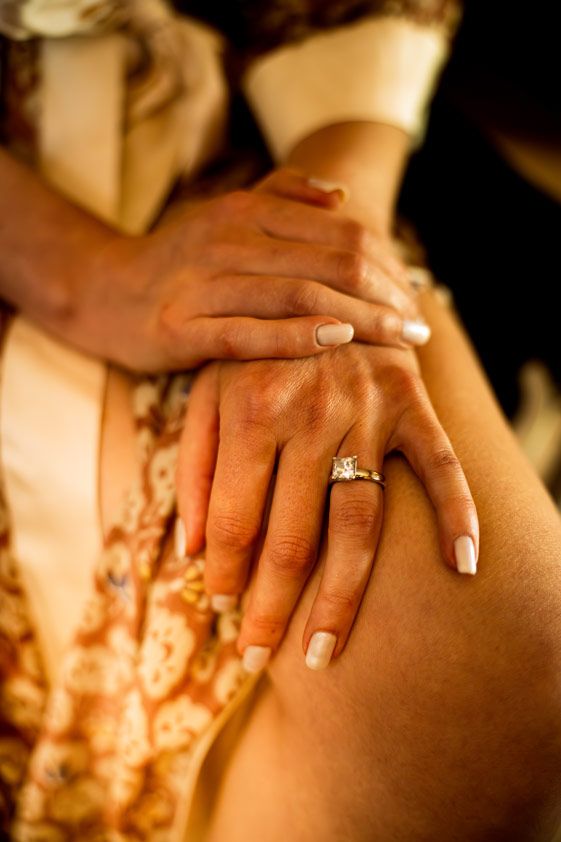 Close-up of hands showing engagement ring in warm lighting.