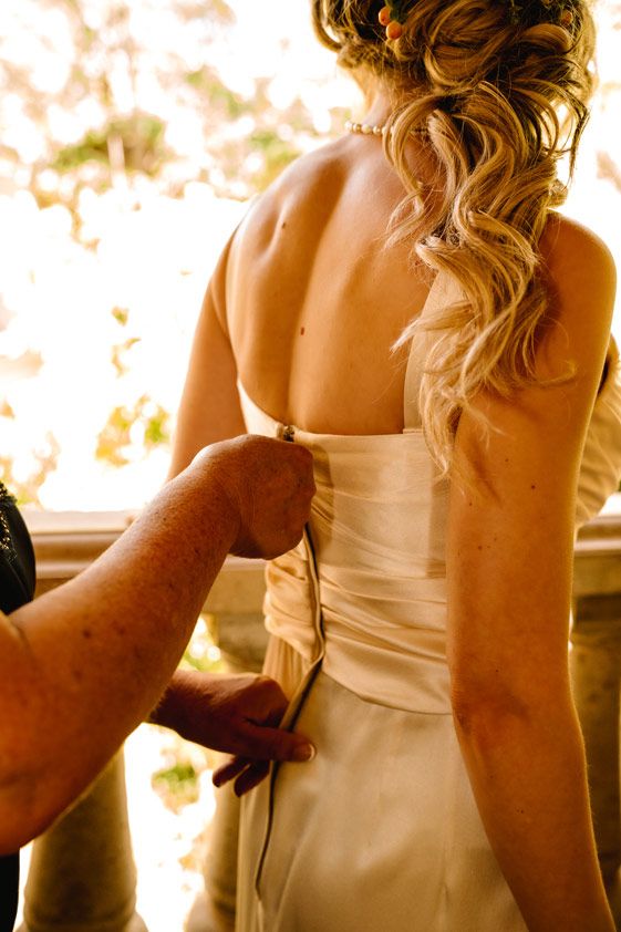 Wedding dress being buttoned up in warm golden light.