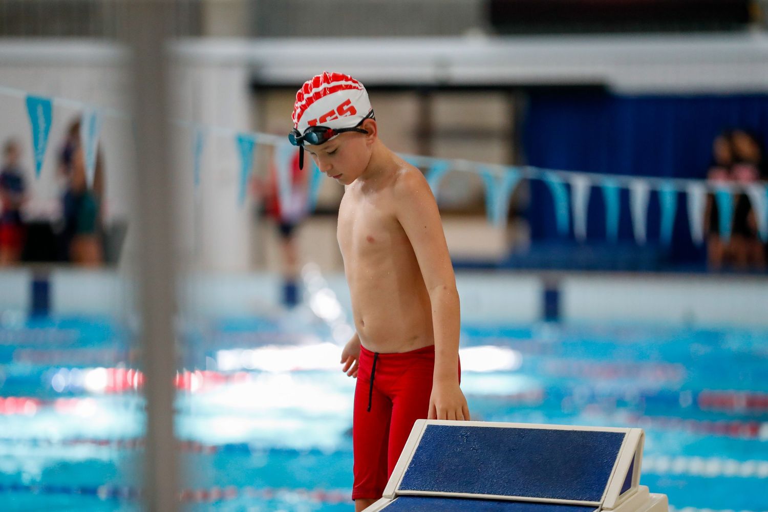 Competitive swimmer in red swim trunks standing by pool edge during training.