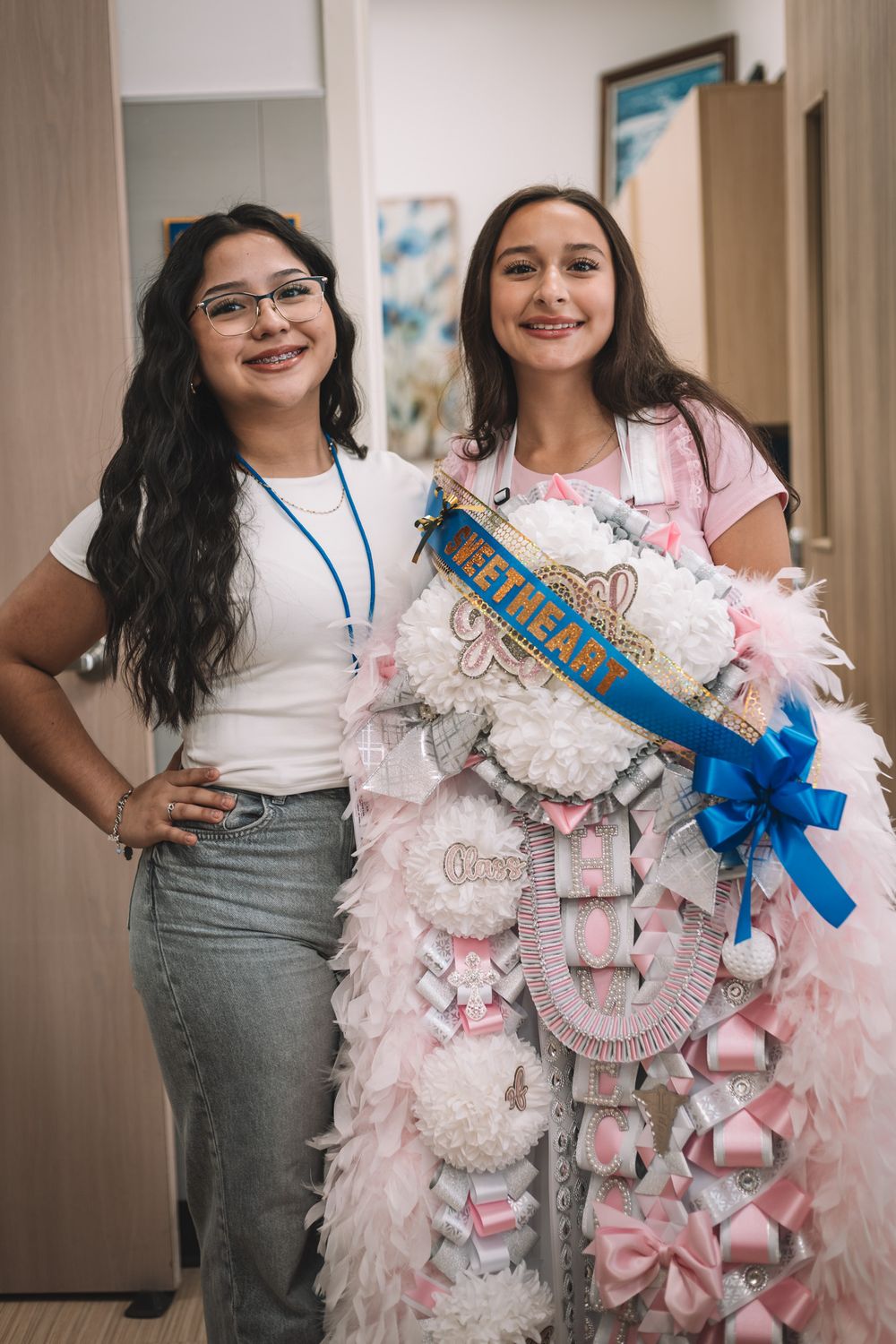 Students display homecoming mums decorated with pink ribbons and blue sashes.