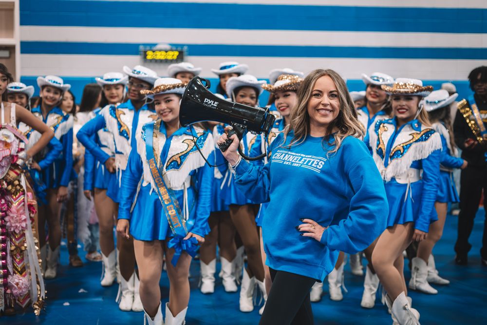 High school marching band members perform in bright blue uniforms during a football game.
