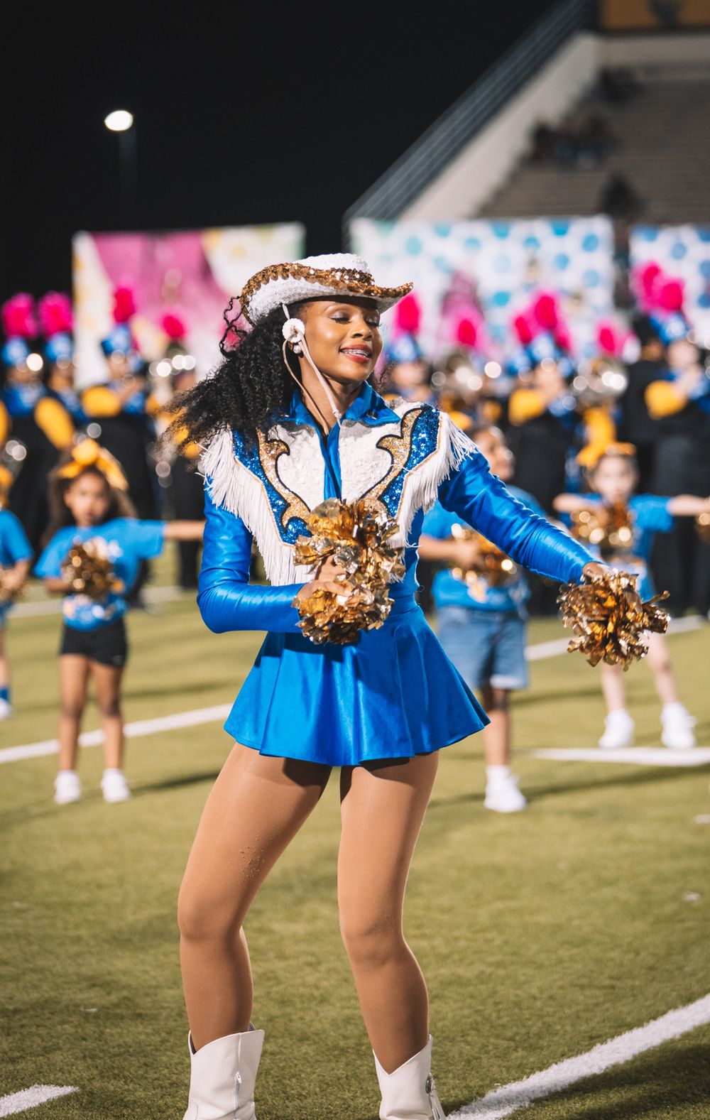 Cheerleaders in bright blue uniforms perform synchronized dance moves on a football field.