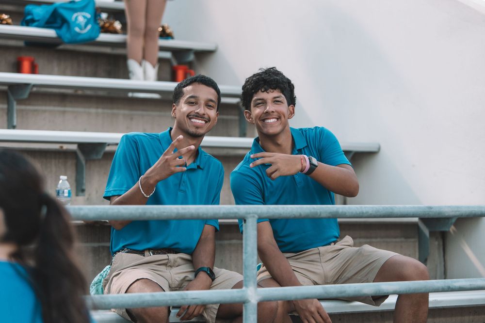 Students in matching blue uniforms share laughs and smiles while sitting together on bleachers.