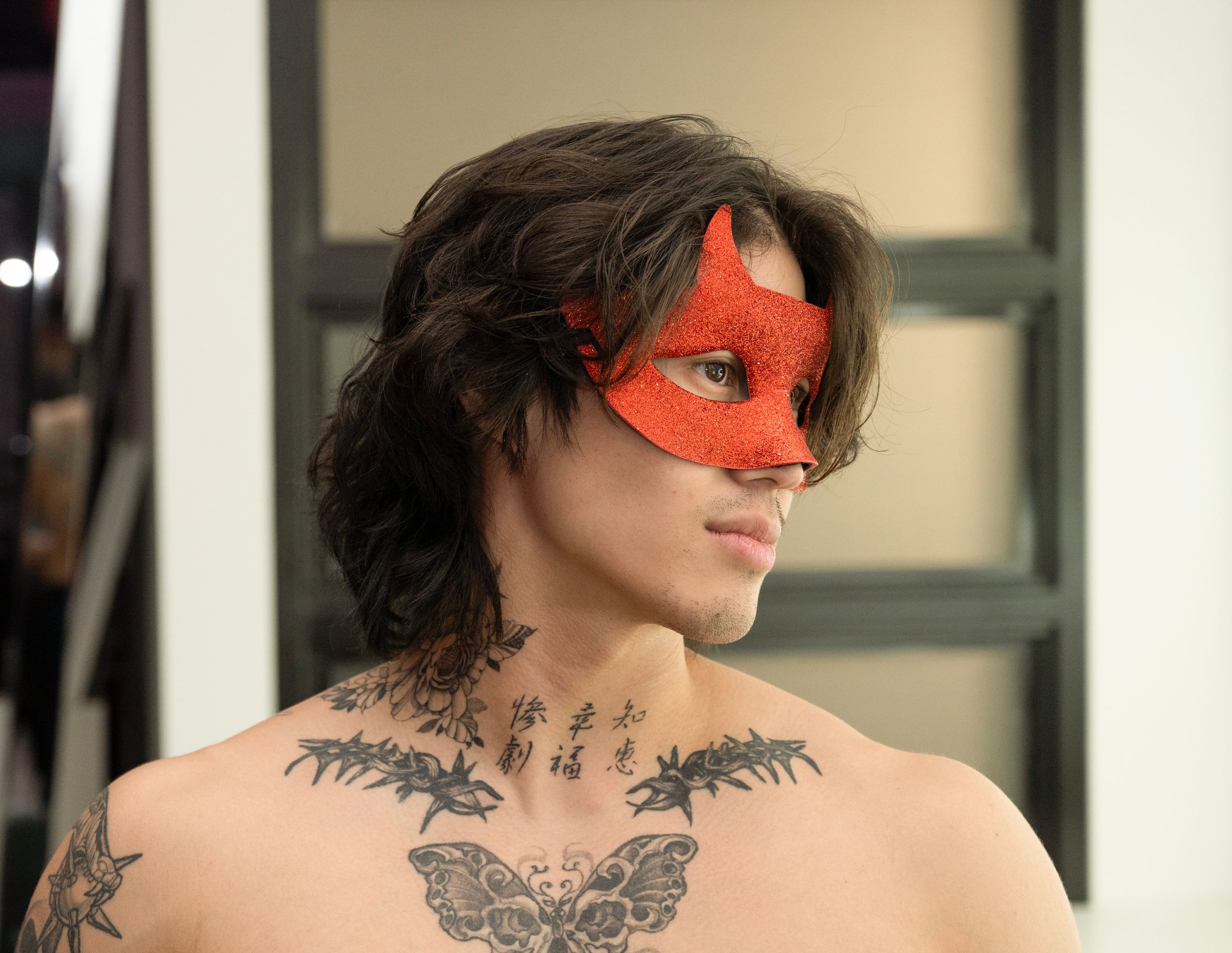 Noire. A beautiful shirtless man with tatoos and a red mask stares longingly toward his left.