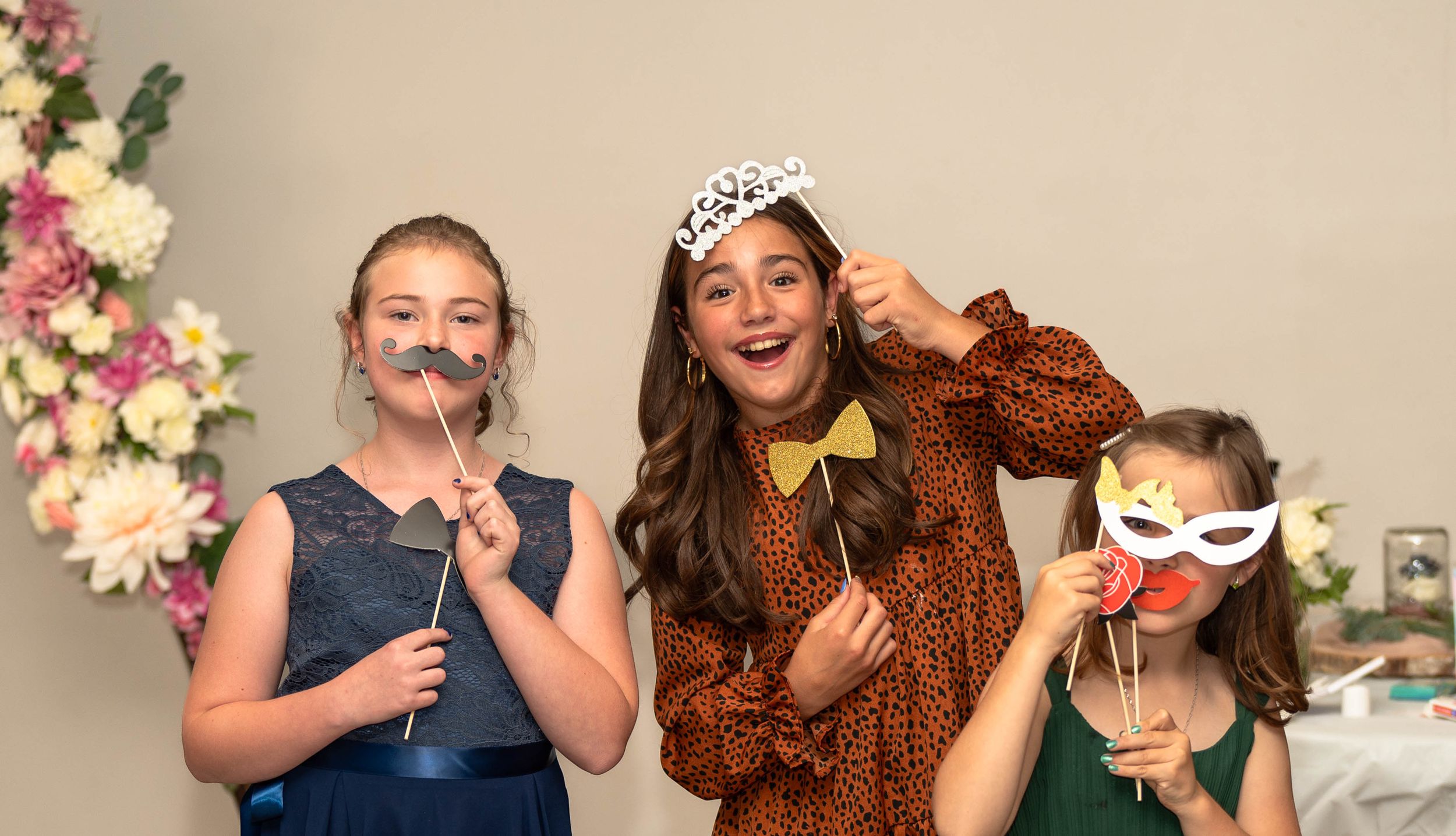 Three girls with masks, mustaches and bow ties giggle for the camera.