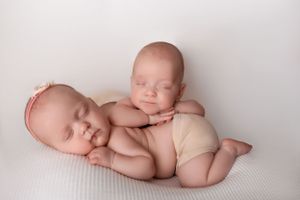 Twin newborn babies in diapers lying close together on a soft white backdrop during a professional photo session in Sussex County NJ