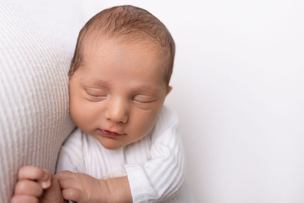Peaceful newborn baby sleeping on soft white blanket during professional photography session.