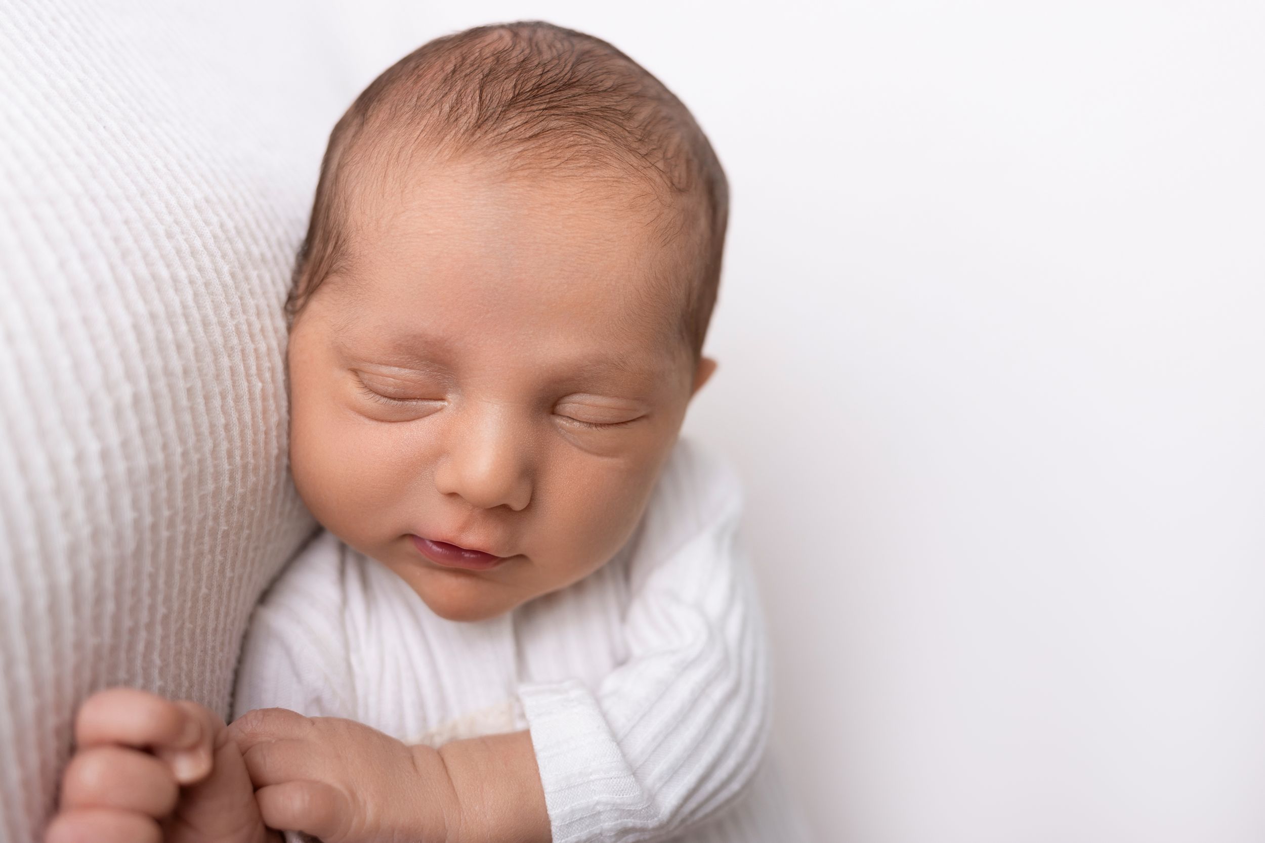 Peaceful newborn baby sleeping on soft white blanket during professional photography session.
