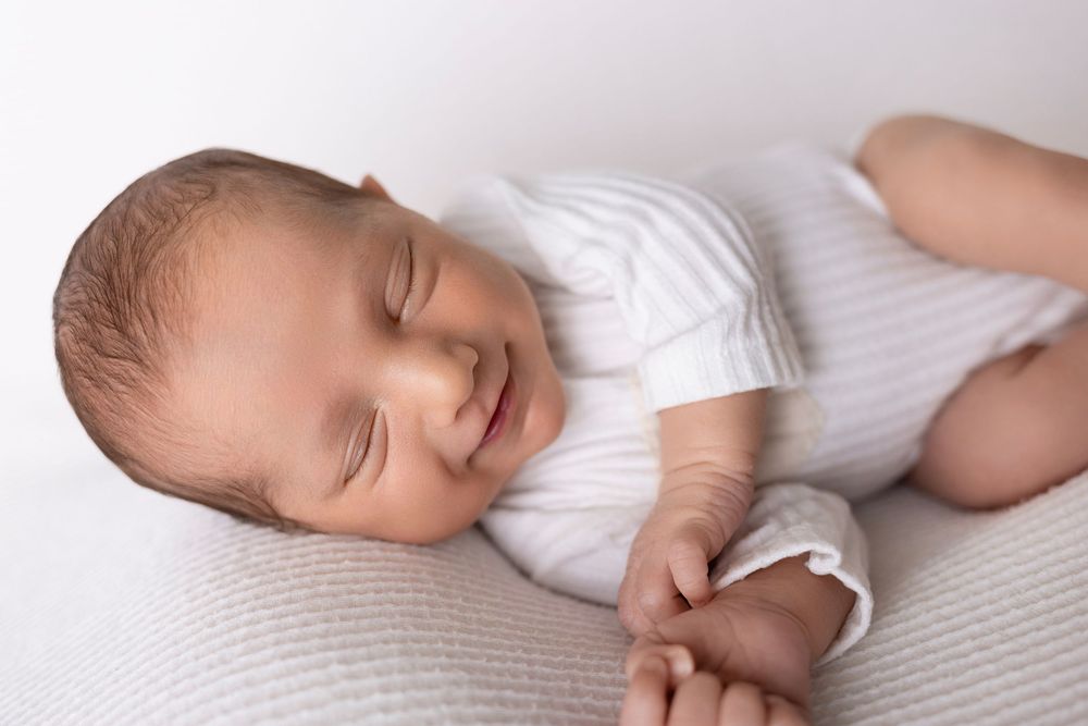 Newborn baby sleeping peacefully on white textured blanket in soft natural light.