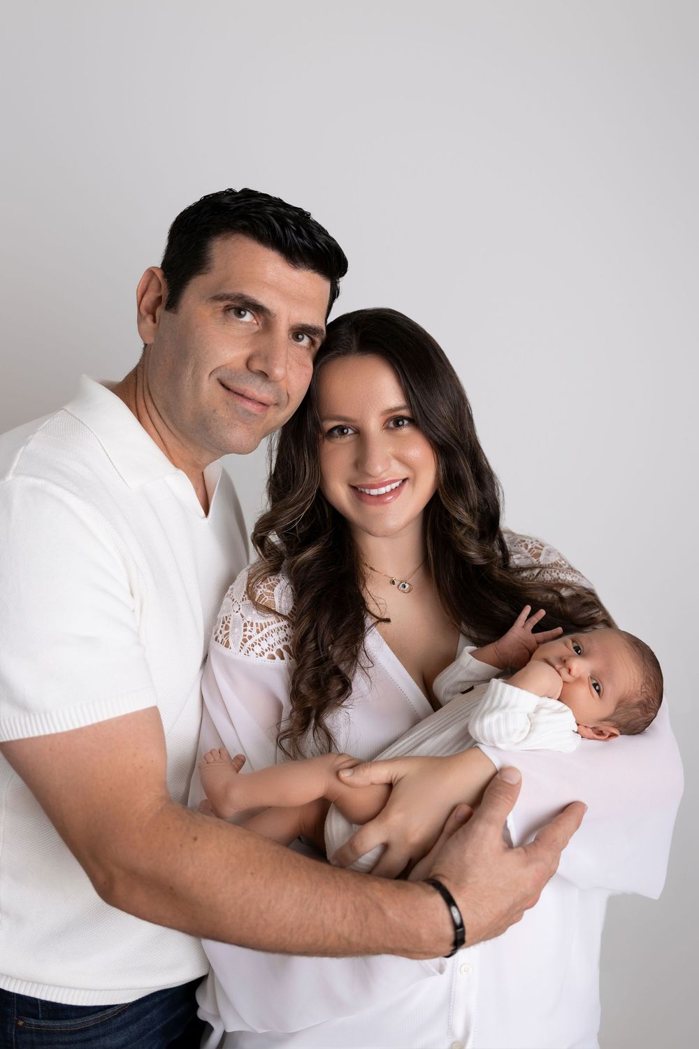 Family portrait series in white clothing against light background showing tender moments with newborn baby.