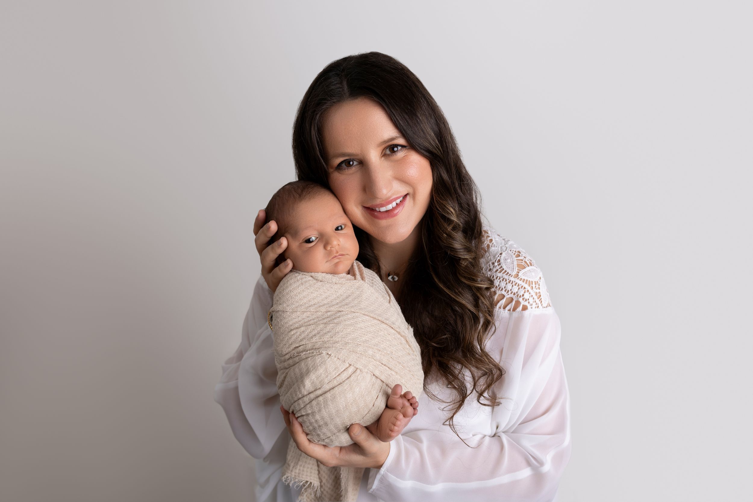 Professional newborn photography session with baby and parent in neutral tones.