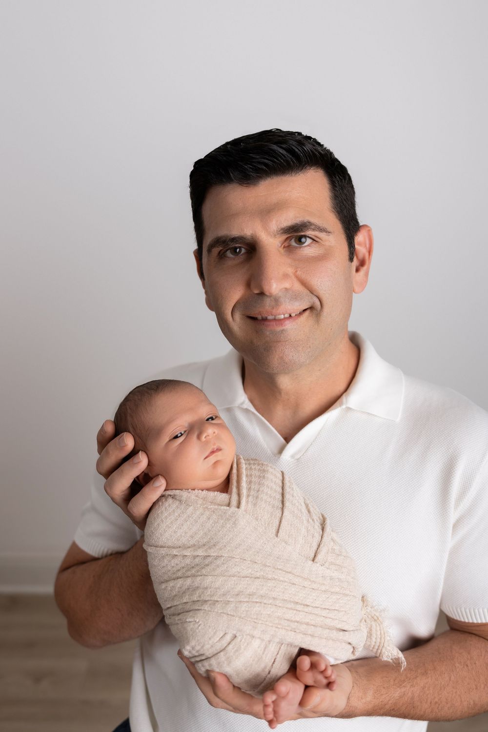 A series of four progressive photos showing a person in white holding a swaddled sleeping baby against their chest.