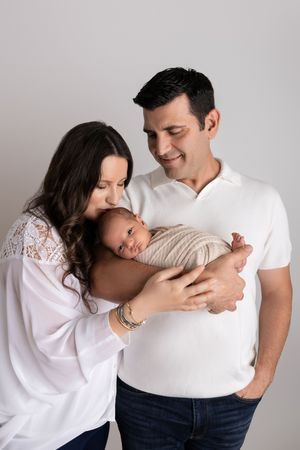 A tender family moment captured as parents gaze adoringly at their swaddled newborn in a studio setting.