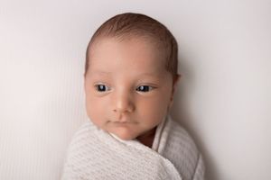 Close-up portrait of sleeping newborn baby wrapped in cream colored swaddle.