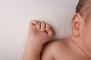Close-up of a tiny newborn's closed fist against a soft white textured background.