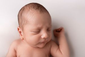 Peaceful sleeping newborn with closed eyes photographed against white fabric in soft lighting.