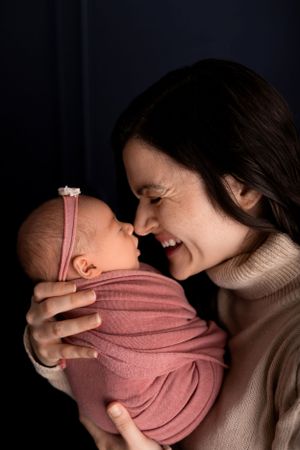 Intimate bonding moment with newborn wrapped in soft pink against dark background.