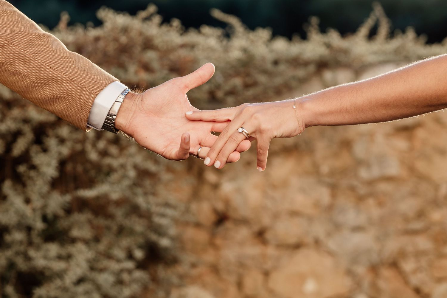 Close-up of hands touching with wedding rings in warm sunlight.