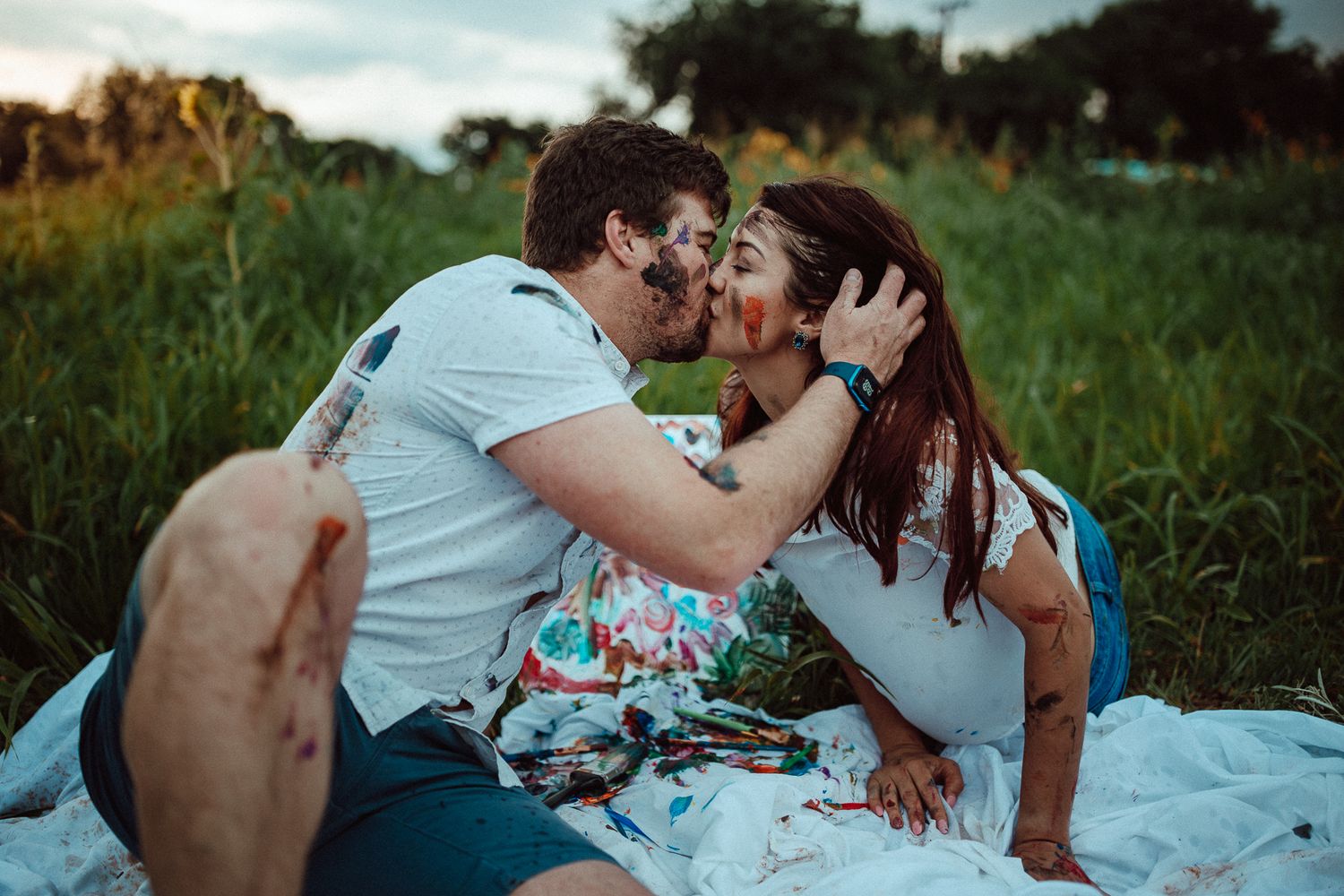 Romantic couple sharing intimate moment on picnic blanket in grassy field at sunset.