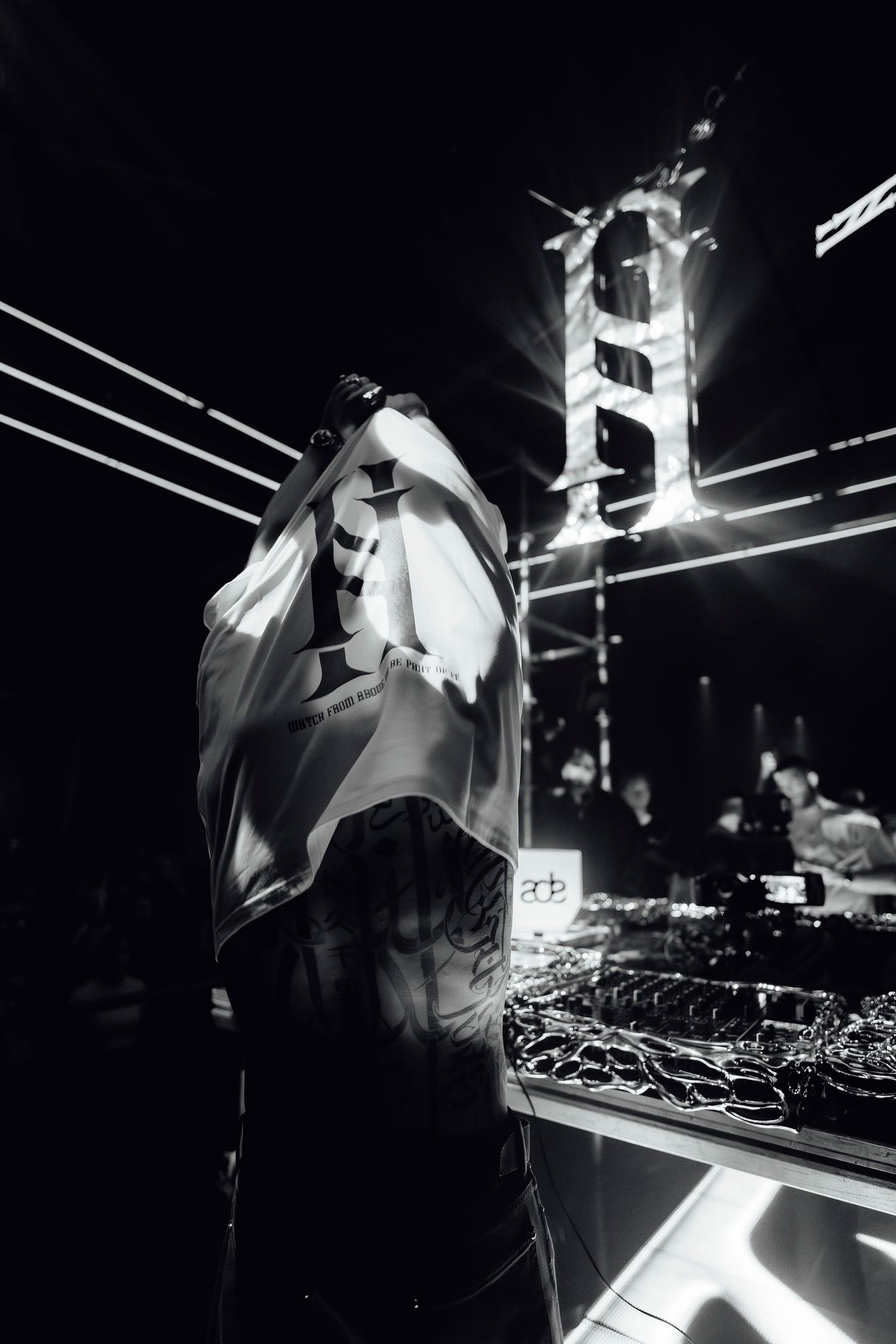 DJ performing behind decks in a dark club with dramatic backlighting.