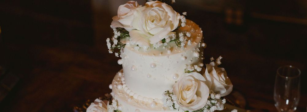 A white three-tiered wedding cake decorated with delicate white roses and floral accents on a dark wooden surface.