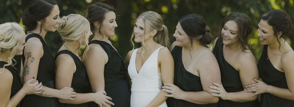 Wedding party members stand in a line wearing black and white formal attire.