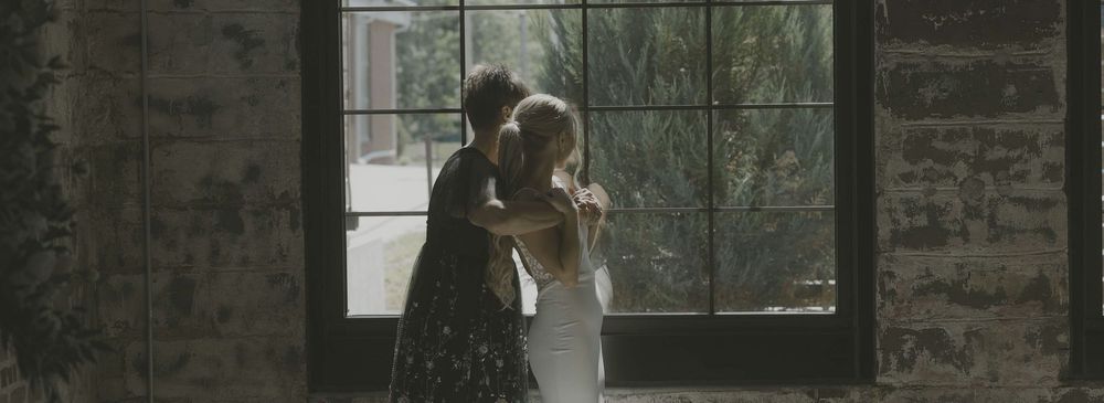 Wedding party stands in front of a stone wall and glass windows during an outdoor celebration.