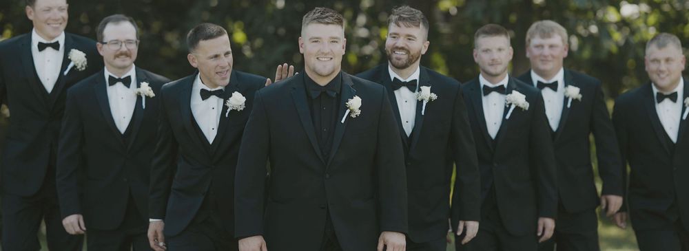 Wedding party members in formal black tuxedos walking together outdoors.