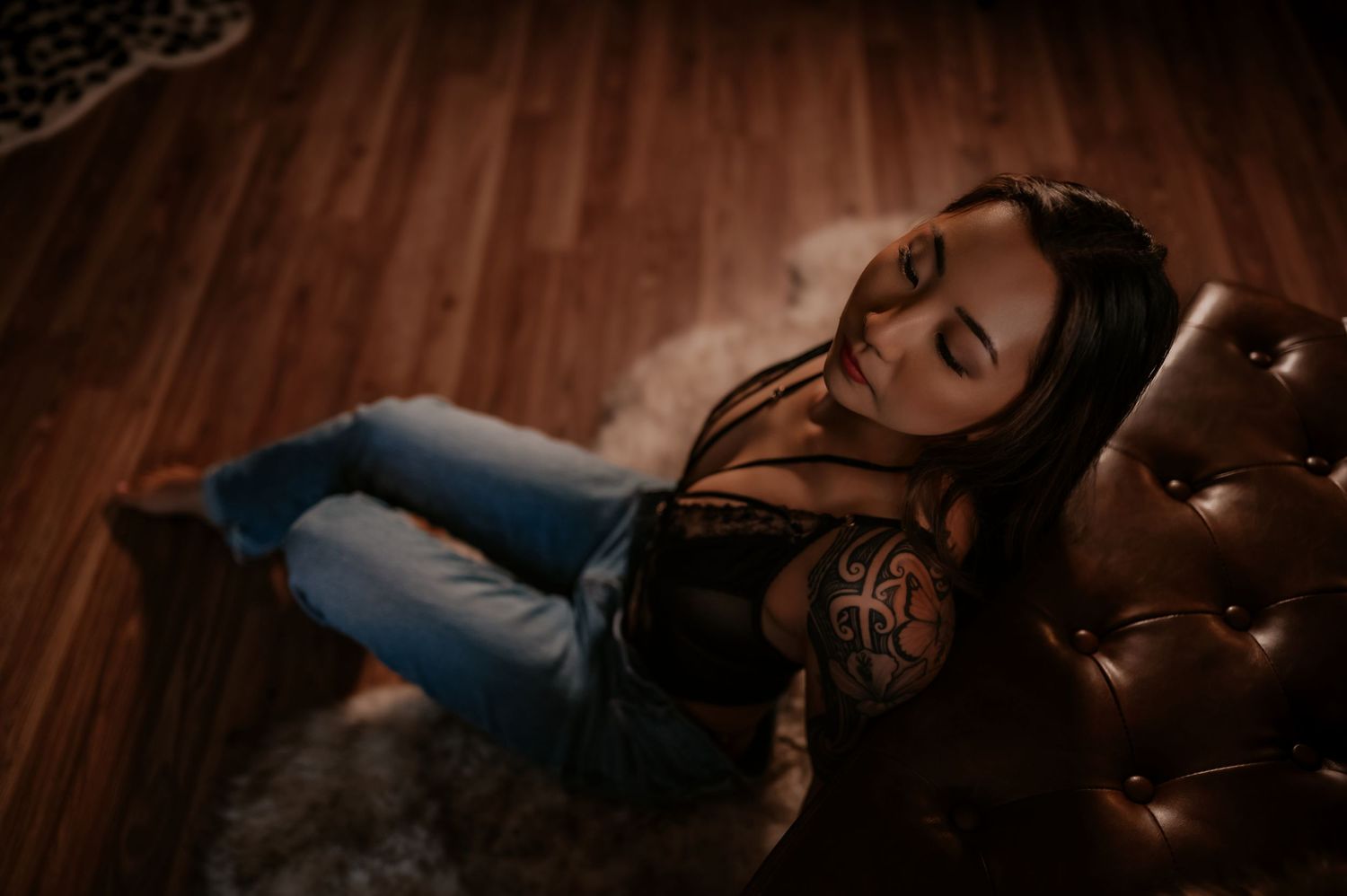 Moody boudoir photo on leather furniture with dramatic lighting and lace details.