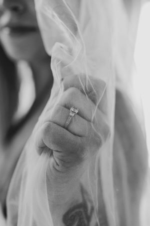 Black and white close-up of tattooed hand with diamond ring holding bridal veil.