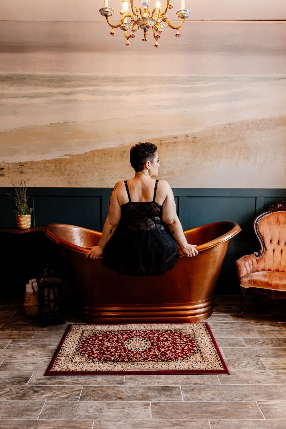 Woman in black lingerie sitting on copper bathtub in elegant vintage-styled room.