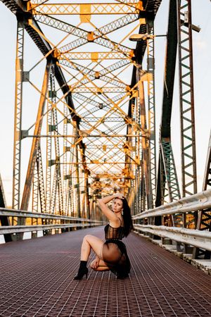 Woman in black bodysuit posing on steel bridge at golden hour.