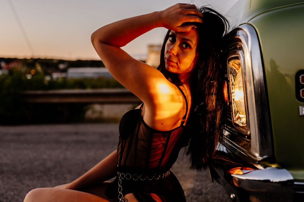 Woman in black corset posing beside vintage green truck at sunset.