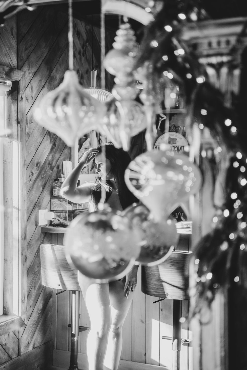 Black and white photo of Christmas ornaments hanging with woman visible in background.