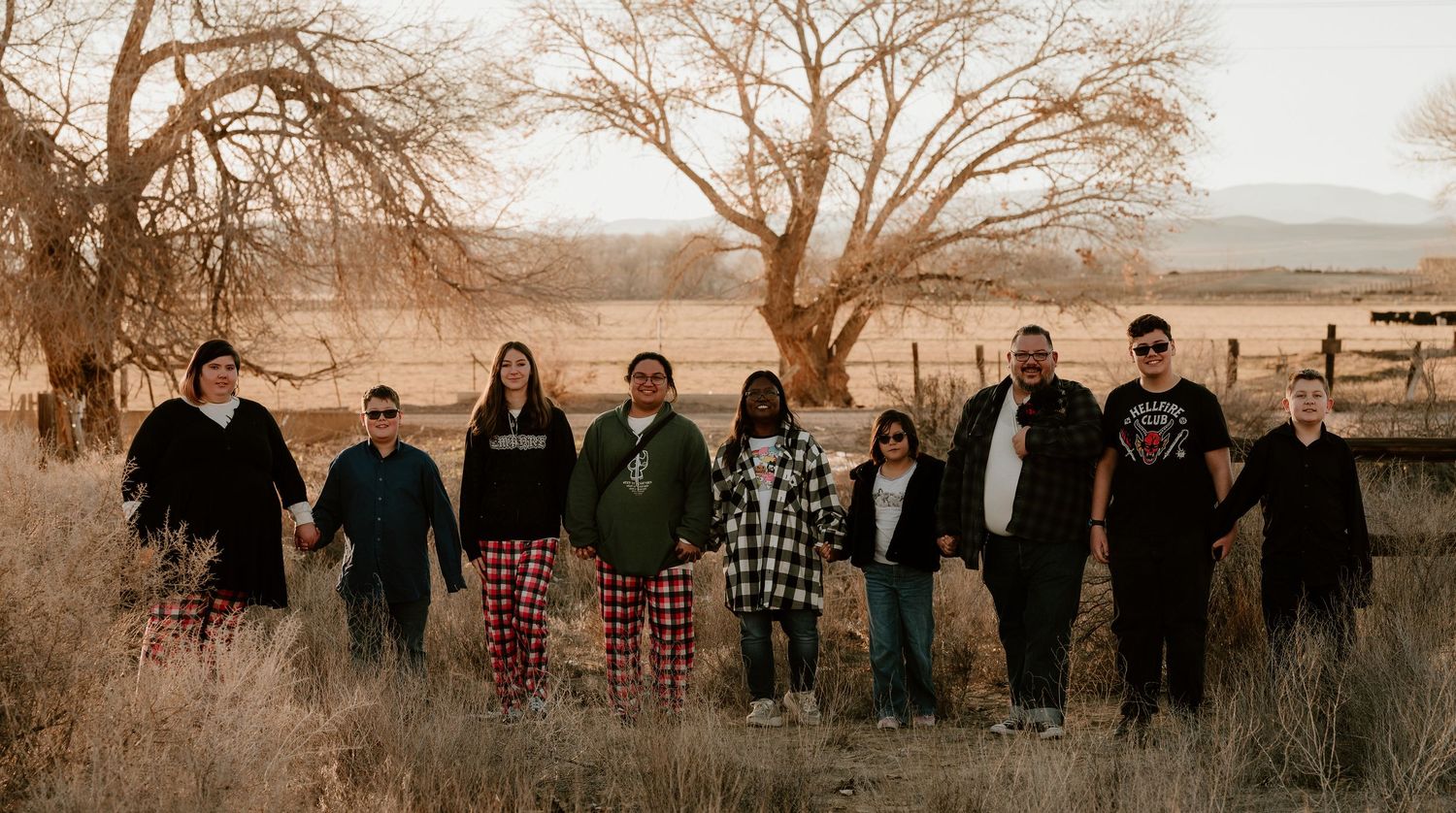 A panoramic sepia-toned image showing a group of people silhouetted against a natural outdoor landscape at sunset.