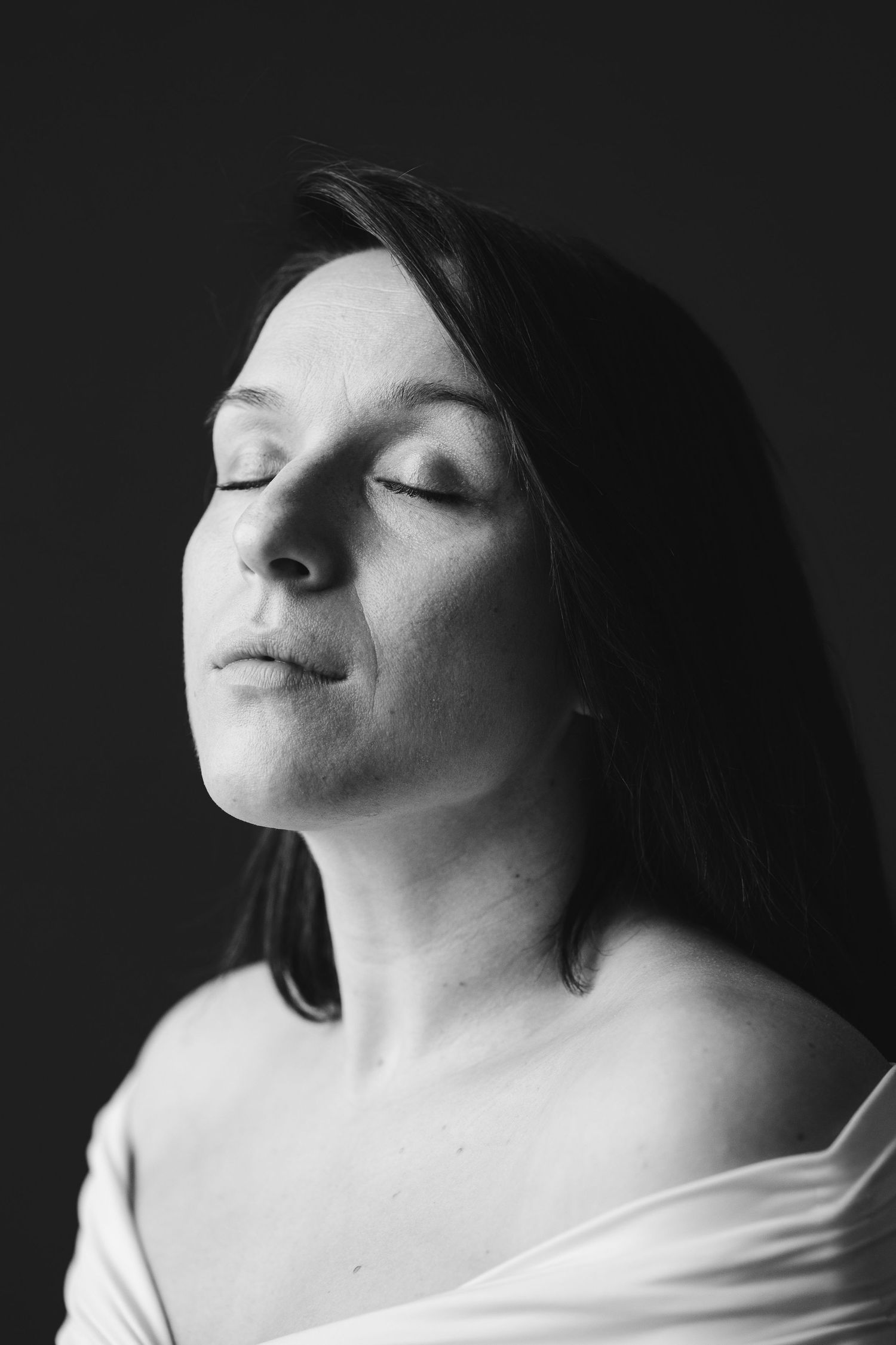 Black and white fine art portrait of a woman in an off-shoulder top with eyes closed taken in a studio in King's Lynn by N-lite photography